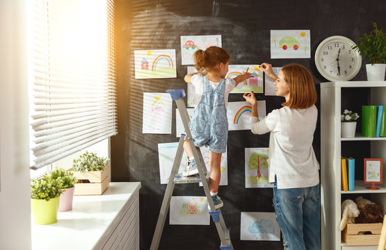 Mother and child girl hang their drawings on wall.