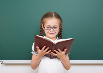 School girl read book, posing at school board, empty space, education concept