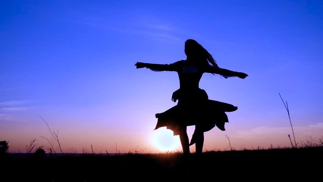 Silhouette of young witch dancing at field