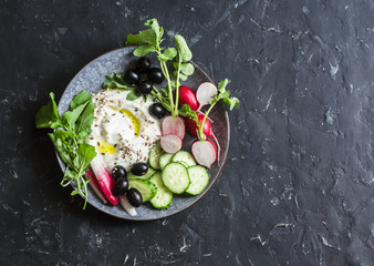 Healthy diet snack in a mediterranean style - greek yogurt, radishes, olives, cucumbers, lettuce on dark background, top view. Flat lay. Copy space