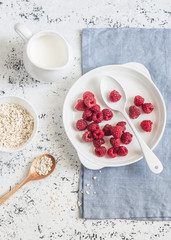 Fresh raspberries, cream and oats on a light background, top view. Delicious breakfast or snack. Flat lay