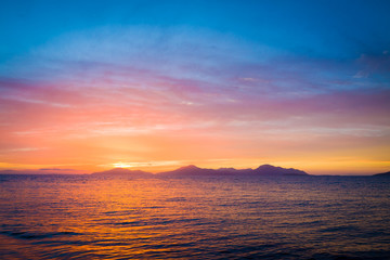 Wonderful sunset behind mountains peak protruding from ocean.
