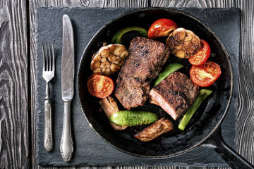 Frying pan with steak and baked vegetables on the table