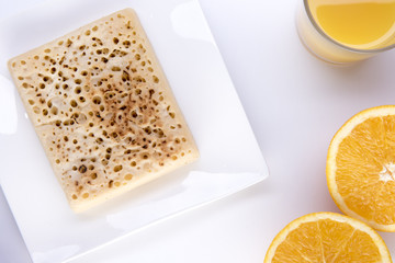 Crumpet on a white plate with orange juice and an orange cut in half 