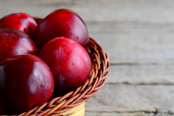Fresh ripe plums in a wicker basket on a vintage wooden background. Plums closeup