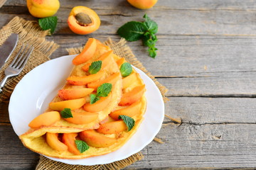 Fruit omelet. Veggie stuffed omelet with fresh apricots on a white plate and an old wooden background with copy space for text. Healthy egg breakfast recipe
