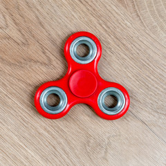 Fidget spinner. Red hand spinner on wooden background.