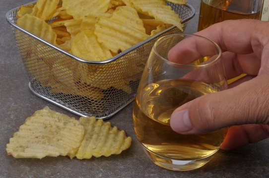 Main prenant un verre de whisky à côté de chips 