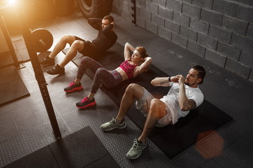 Group of athletic adult men and women performing sit up exercises to strengthen their core abdominal muscles at fitness training - obrazy, fototapety, plakaty