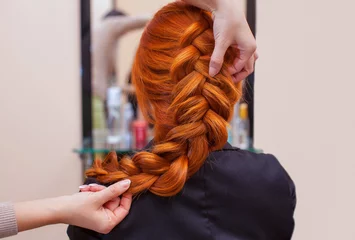 Photo sur Plexiglas Salon de coiffure Beautiful, red-haired girl with long hair, hairdresser weaves a French braid, in a beauty salon. Professional hair care and creating hairstyles.