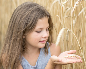 beautiful little girl holding wheat spike on hand palms in field at summer day. Concept of purity, growth, happiness