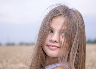 Little girl in golden wheat field in summer day. Portrait of a beautiful child. Concept of purity, growth, happiness