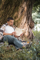 Fototapeta premium The young man at the tree reading a book