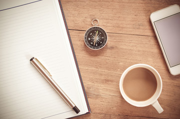 Compass and coffee cup with,smart phone, notepad on wooden table surface background textured,for business and finance concept.