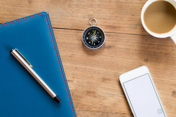 Compass and coffee cup with,smart phone, notepad on wooden table surface background textured,for business and finance concept.