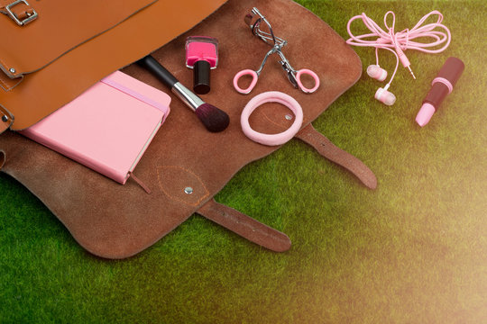 Female fashion accessories - bag, note pad, headphones, lipstick and other essentials on the grass