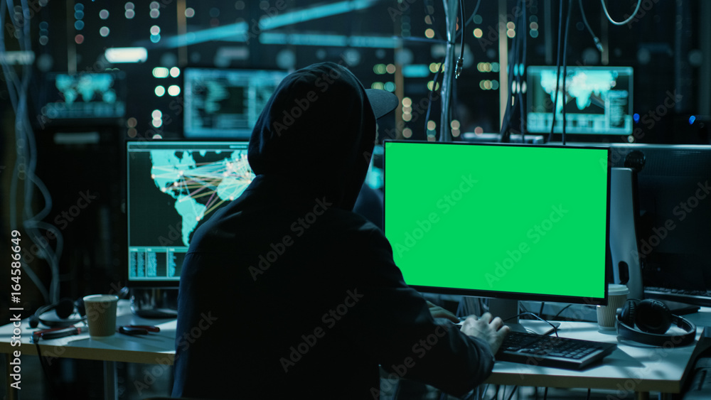 Poster Teenage Hacker is Working With his Computer with Green Screen Mock-up Display Infect Servers and Infrastructure with Malware. His Hideout is Dark, Neon Lit and Has Multiple displays.