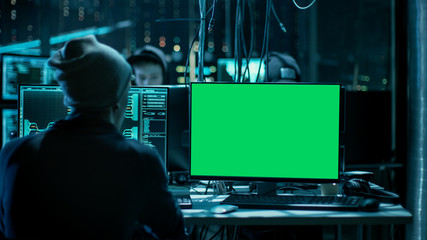 Shot of Teenage Hacker Working with Green Screen Mock-up Display Infecting Servers and Infrastructure with Malware. His Hideout is Dark, Neon Lit and Has Multiple Displays. Good as a Template.