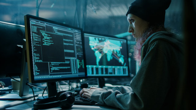 Nonconformist Teenage Hacker Girl Using her Computer to Organize Malware Attack on Global Scale. She's in Underground Secret Location Surrounded by Displays and Cables.