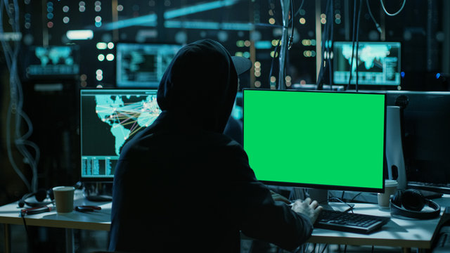 Teenage Hacker is Working With his Computer with Green Screen Mock-up Display Infect Servers and Infrastructure with Malware. His Hideout is Dark, Neon Lit and Has Multiple displays.