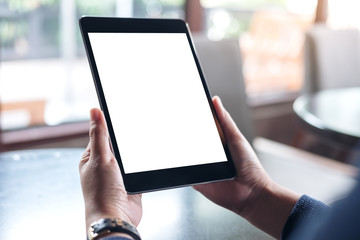 Mockup image of hands holding black tablet pc with white blank screen in modern cafe