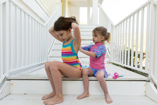 Girl applying suntan lotion to her sister while sitting on the steps