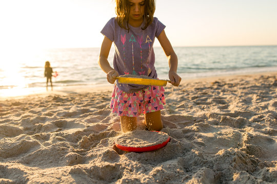 Girls playing with sand and frisbee on beach at sunset 