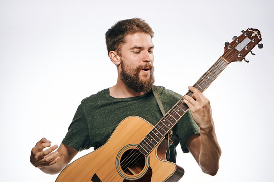 Young guy with a beard on a light background holds a guitar