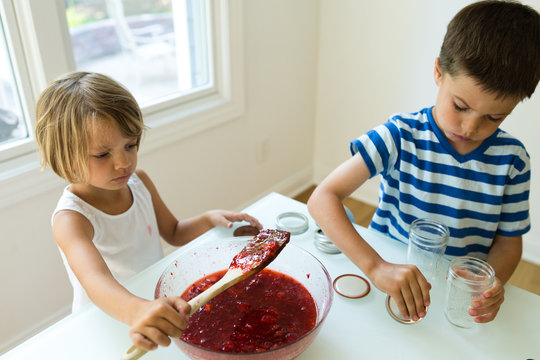 Boy and girl preparing to pour freshly made jam into jars