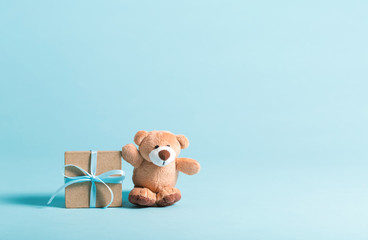 Baby birthday theme with teddy bear and gift box on a blue background - obrazy, fototapety, plakaty