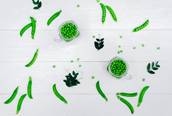 Full glass jar with fresh green peas on white wooden background, top view. Bio healthy food. Green peas in jar, pods and pea leaves on wooden table