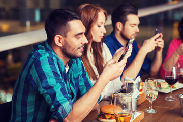 friends with smartphones dining at restaurant