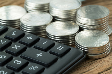 selective focus on calculator with stack of coins in the background on wood table as financial saving concept