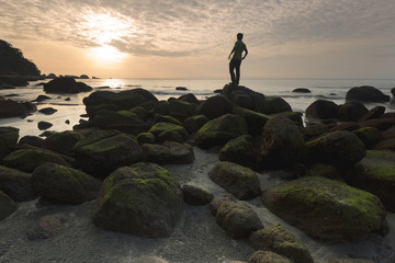 A young traveler standing among rocks at a beautiful beach. The rock is covered by green mosses. This is a travel and active lifestyle concept, exploring Asia.