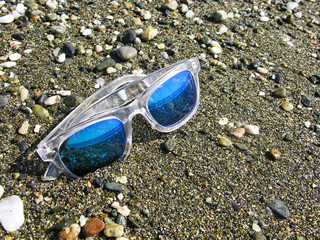 Fototapeta na wymiar Top view of sunglasses on the beach near the blue sea with sand.