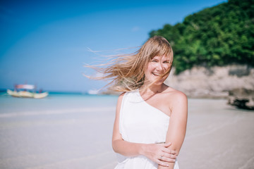Portrait of the beautiful blond long hair woman dancing on the beach. Happy island lifestyle. White sand, blue cloudy sky and crystal sea of tropical beach. Vacation on the paradise island
