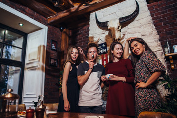 Group of young people posing at camera standing, smiling, laughing, making faces while having fun in trendy restaurant