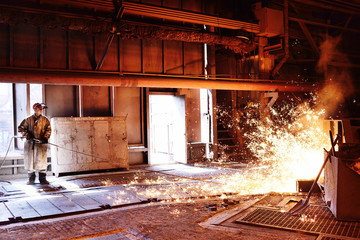 Fototapeta na wymiar Liquid metal is poured into molds. Worker, controlling the melting of metal in furnaces. A man works at a metallurgical plant against a blast furnace