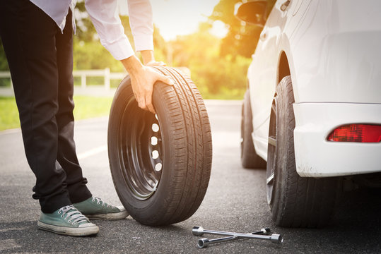 Asia Man With A White Car That Broke Down On The Road.Changing Tire On Broken Car On Road.