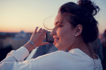 young girl is shooting the city view by the phone and smiling