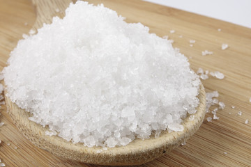 Close up of salt on wooden spoon over wooden background.