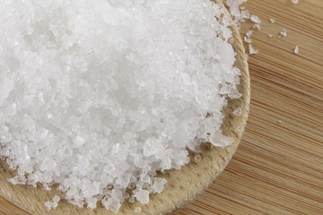 Close up of salt on wooden spoon over wooden background.