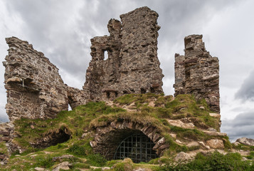 Assynt Peninsula, Scotland - June 7, 2012: Full frame closeup of Brownish Ruins of Castle Ardvreck with cellar grill. Green ground vegetation. Silver sky.