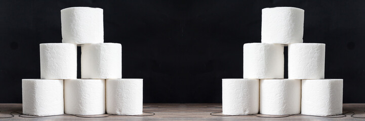 Stack of toilet paper rolls on wooden table against black background. Copy space. Wide panoramic image. 