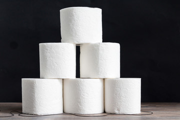 Stack of toilet paper rolls on wooden table against black background. Copy space.