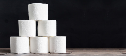 Stack of toilet paper rolls on wooden table against black background. Copy space. Wide panoramic image.