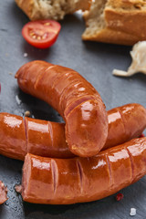 Grilled Sausages on a black stone plate on white wooden table with tomatoes, garlic, salt and pepper