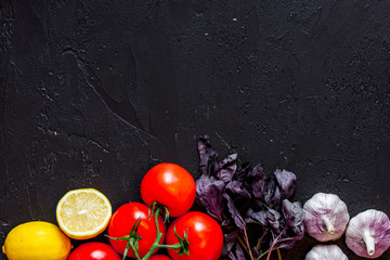 Cook workplace. Tomato, garlic, lemon on black table background top view copyspace