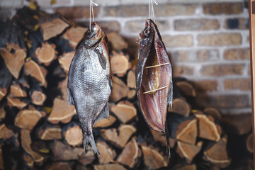 Two large smoked fish hang on background of stacked firewood