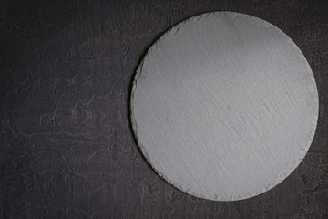 Empty round slate serving dish on a black stone background